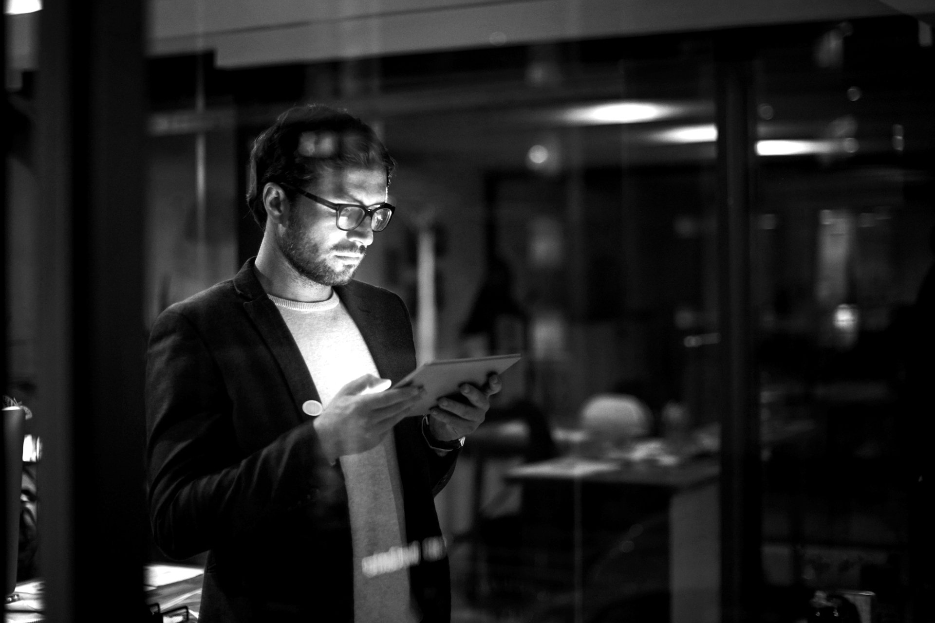 Mann liest im modernen Büro bei Nacht einen Blogbeitrag auf dem Tablet zur beruflichen Weiterbildung.